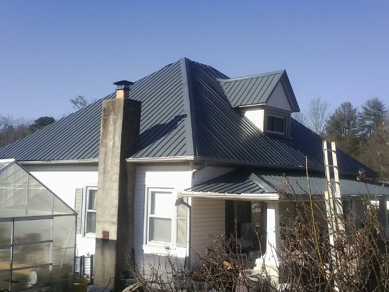 Dark blue standing seam metal roof on a white farmhouse with dormer — Slate & Tile Roof Repair by Roofing Brothers in Erwin