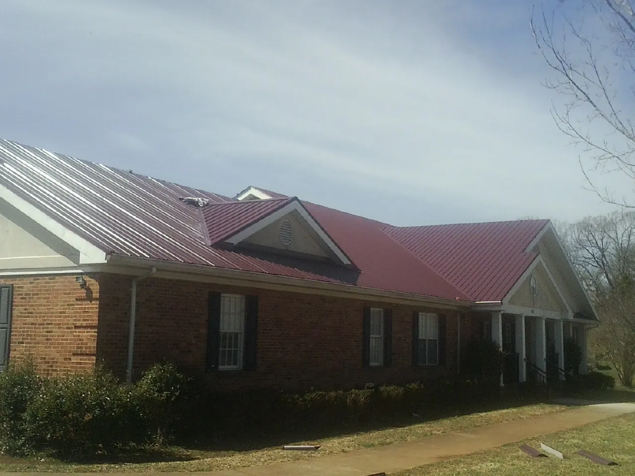 Red metal roof with gabled entries on a long brick building, from a Hail Damage Roof Repair job in Erwin