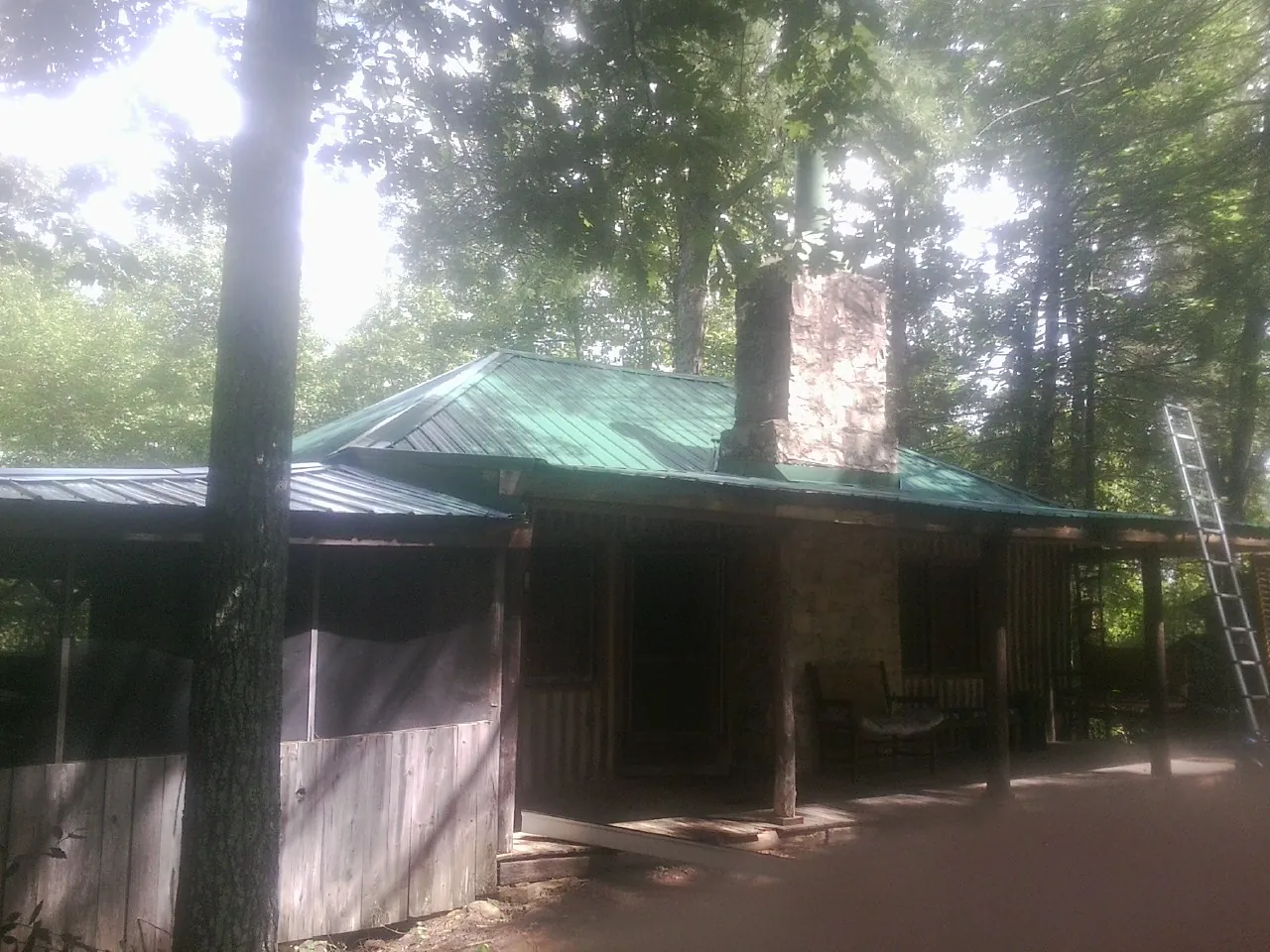 Green metal roof and stone chimney above a log cabin porch in Erwin