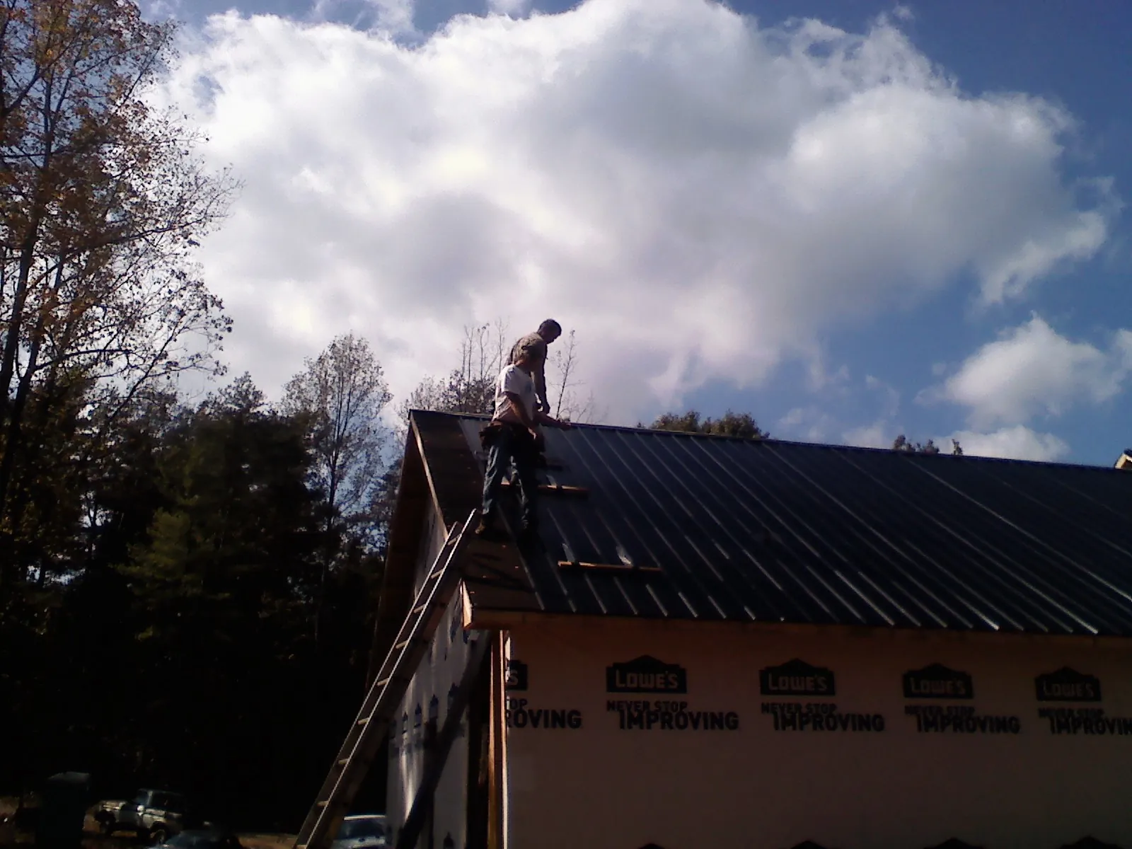 Roofer fastening dark metal panels high against a cloudy sky, from a Roof Inspection job in Erwin